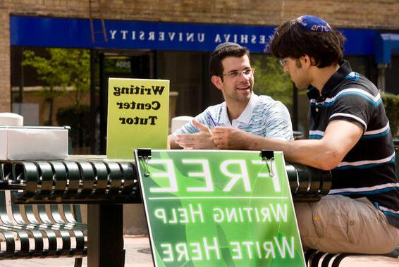 two men sitting at a table with a sign for free writing help